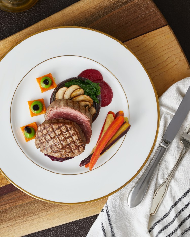 A beautifully plated gourmet meal featuring a seared and sliced piece of beef filet, accompanied by colorful vegetable garnishes and sauces on a white plate, with a wooden cutting board in the background. Private Chef Collingwood, Private Chef Toronto